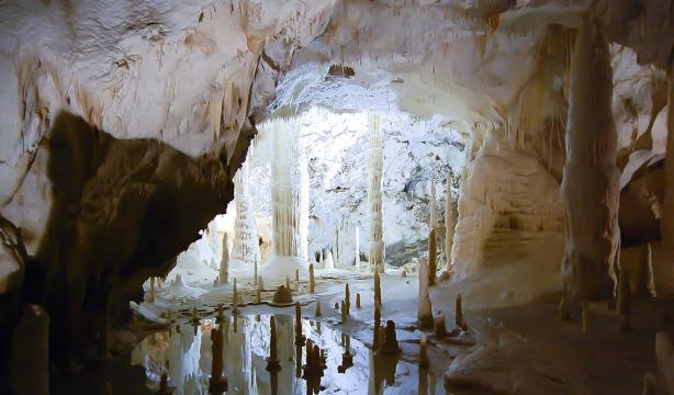 Majestic cave with stalactites and stalagmites reflecting in crystal-clear water.